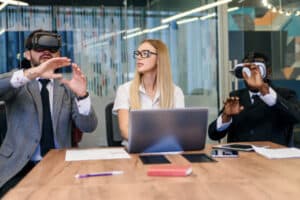 3 people in a meeting sitting at a desk and 2 of them are using VR
